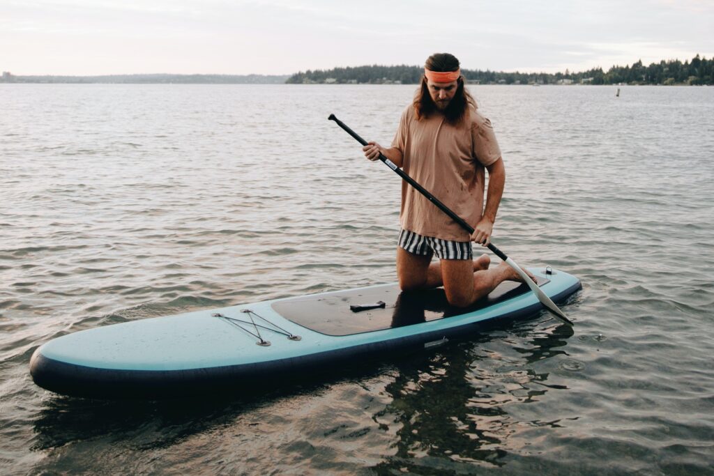 A man holding a paddle board, wondering if weight affects paddle boarding.